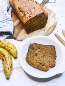Banana bread loaf with a slice of banana bread and banana in the foregound