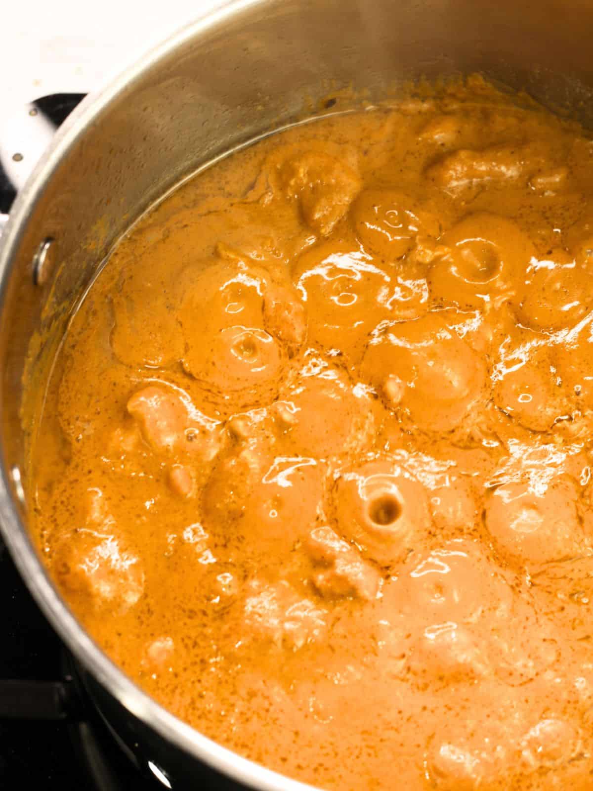 Pot with bubbling butter chicken curry in it